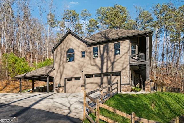 chalet / cabin featuring concrete driveway, a balcony, stone siding, an attached garage, and a front lawn