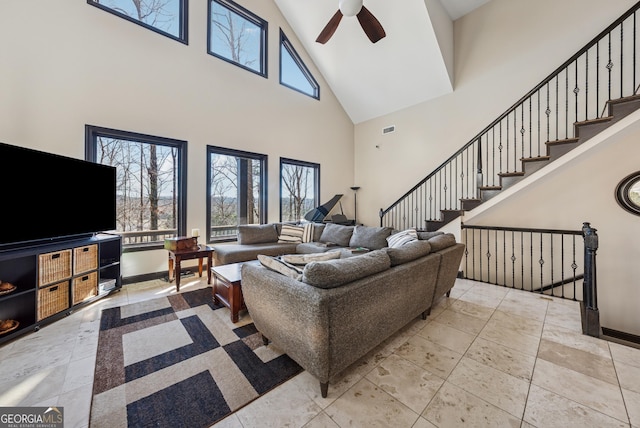 living area featuring ceiling fan, a towering ceiling, visible vents, baseboards, and stairway