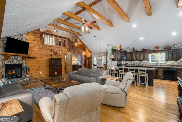 living room featuring a ceiling fan, wooden walls, a fireplace, light wood finished floors, and stairs