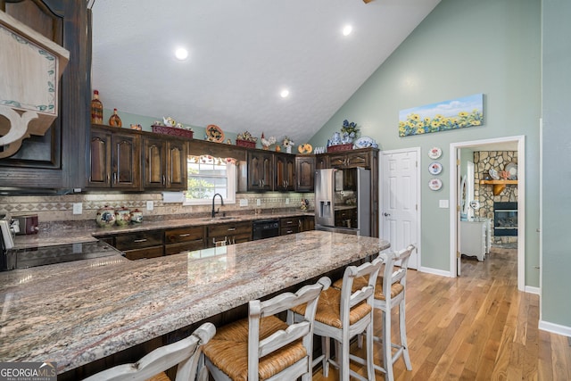 kitchen with a peninsula, a sink, dark brown cabinetry, black dishwasher, and stainless steel fridge