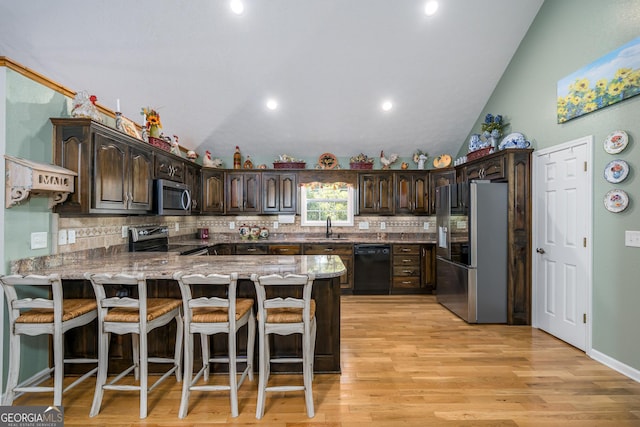 kitchen featuring a breakfast bar area, a peninsula, a sink, stainless steel appliances, and dark brown cabinetry