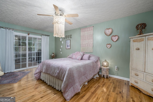 bedroom with access to exterior, a textured ceiling, baseboards, and wood finished floors