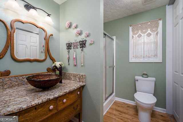 full bathroom with vanity, wood finished floors, a textured ceiling, toilet, and a shower with door