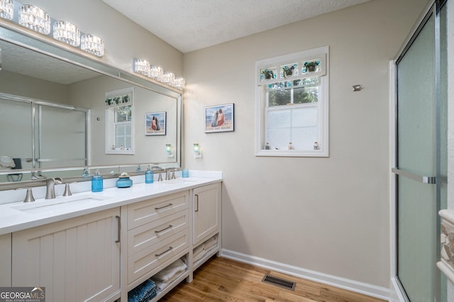 bathroom featuring visible vents, a sink, wood finished floors, a shower stall, and double vanity