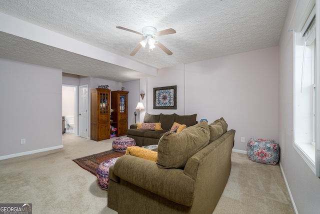 living area featuring baseboards, light colored carpet, a ceiling fan, and a textured ceiling