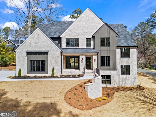 modern farmhouse style home featuring roof with shingles, brick siding, and board and batten siding