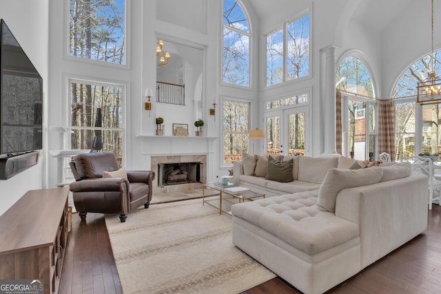 living room with an inviting chandelier, a high ceiling, a high end fireplace, french doors, and wood-type flooring