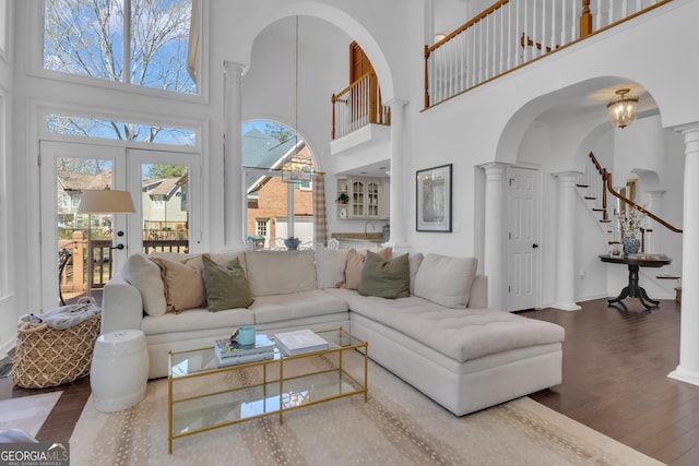 living area with stairway, french doors, wood finished floors, arched walkways, and ornate columns