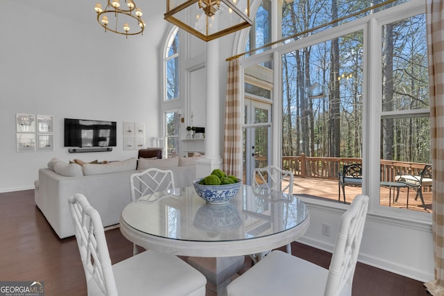 dining area with dark wood-style floors, baseboards, ornate columns, a towering ceiling, and a notable chandelier