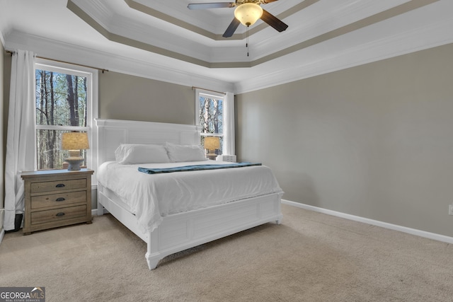 carpeted bedroom featuring a ceiling fan, a tray ceiling, crown molding, and baseboards