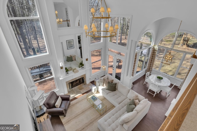 living area featuring a tiled fireplace, wood finished floors, an inviting chandelier, and a towering ceiling