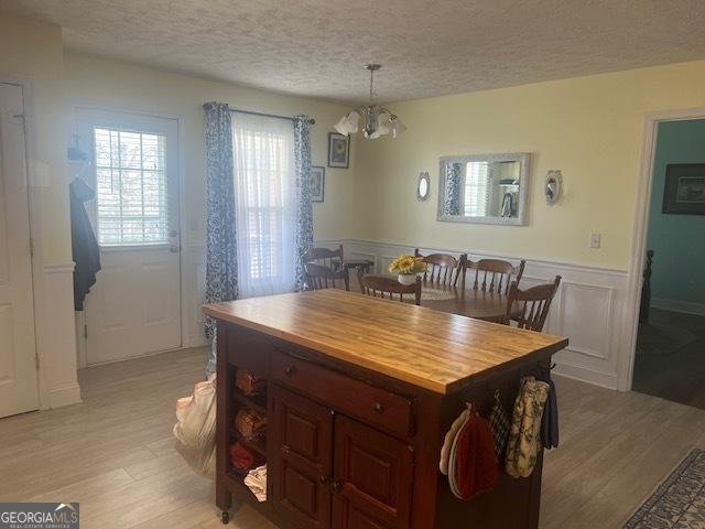 dining area with a textured ceiling, light wood finished floors, wainscoting, and a chandelier