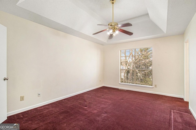 carpeted empty room with ceiling fan, a raised ceiling, baseboards, and a textured ceiling