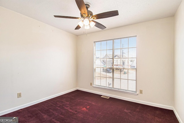 empty room with dark colored carpet, visible vents, baseboards, and a ceiling fan