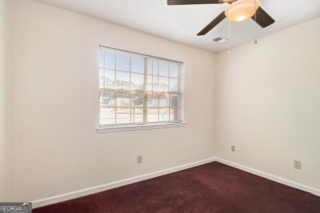 spare room with baseboards, visible vents, dark carpet, and ceiling fan