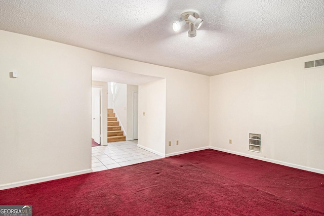 carpeted spare room featuring tile patterned flooring, visible vents, baseboards, stairs, and a textured ceiling