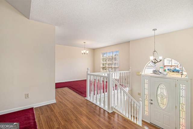 entrance foyer with a textured ceiling, wood finished floors, baseboards, and a chandelier