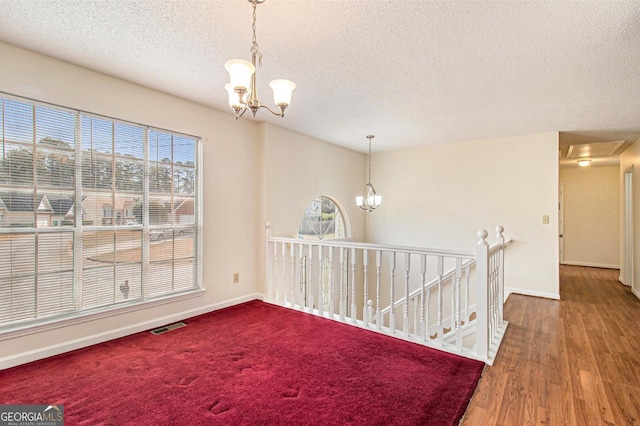 empty room with an inviting chandelier, a healthy amount of sunlight, baseboards, and a textured ceiling