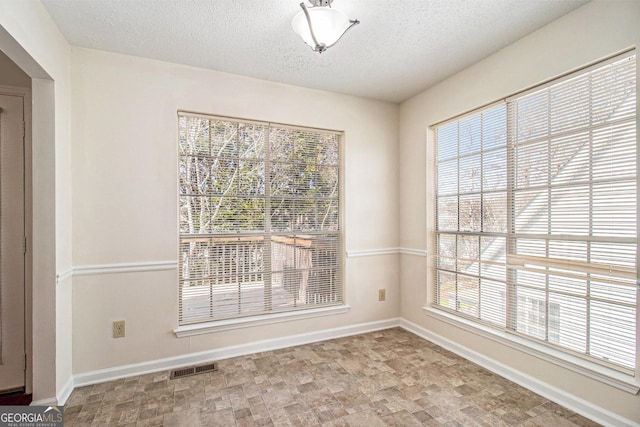 empty room featuring visible vents, a textured ceiling, and baseboards