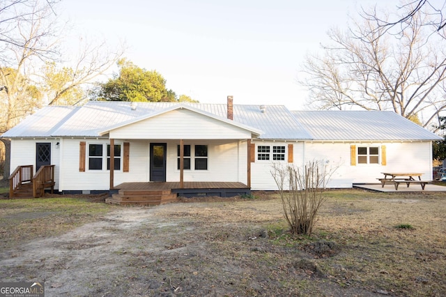 view of front of home featuring metal roof, a porch, a chimney, and a patio