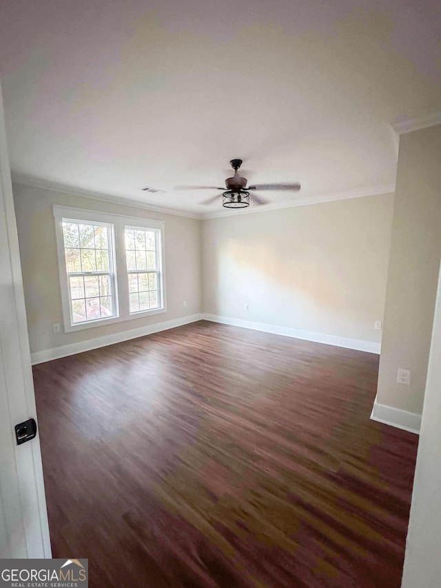 unfurnished room featuring dark wood-style flooring, a ceiling fan, baseboards, visible vents, and crown molding