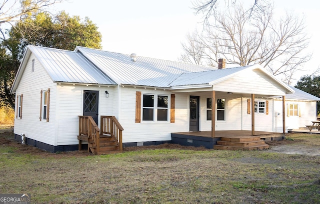 view of front facade with covered porch, metal roof, a chimney, and a front lawn