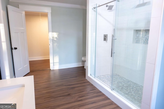 bathroom featuring a stall shower, baseboards, toilet, ornamental molding, and wood finished floors