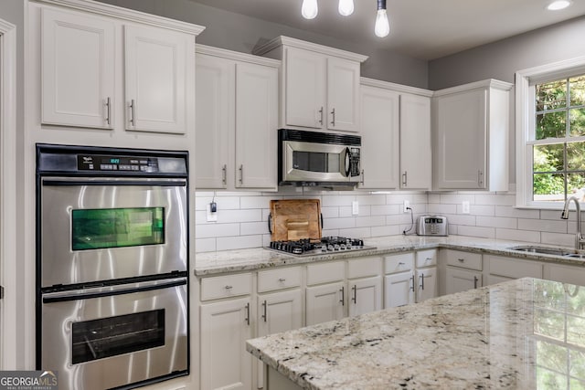 kitchen with light stone countertops, a sink, stainless steel appliances, white cabinetry, and backsplash