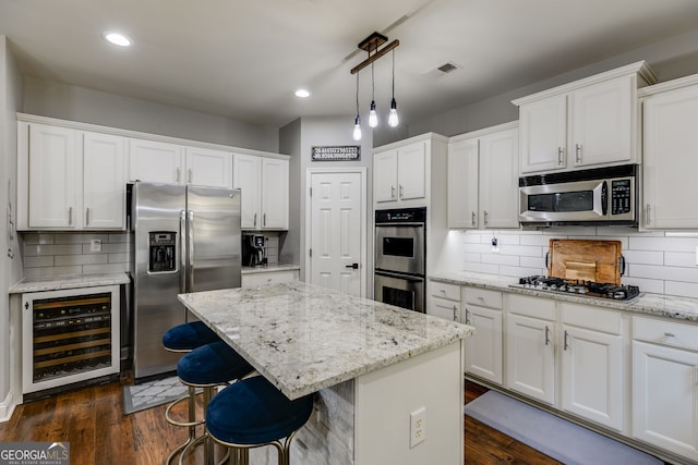 kitchen featuring dark wood-type flooring, beverage cooler, a center island, white cabinetry, and appliances with stainless steel finishes