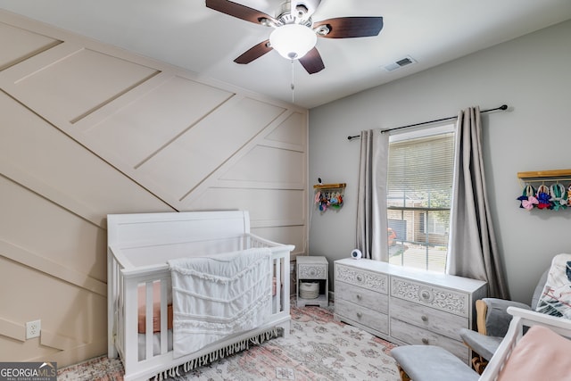 bedroom with visible vents, a crib, and ceiling fan