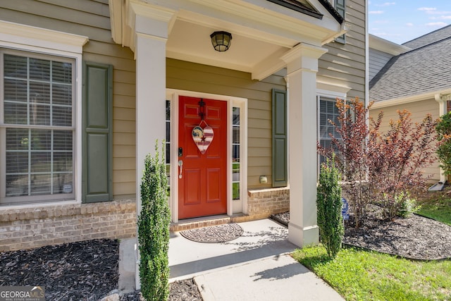 property entrance with a porch, brick siding, and roof with shingles