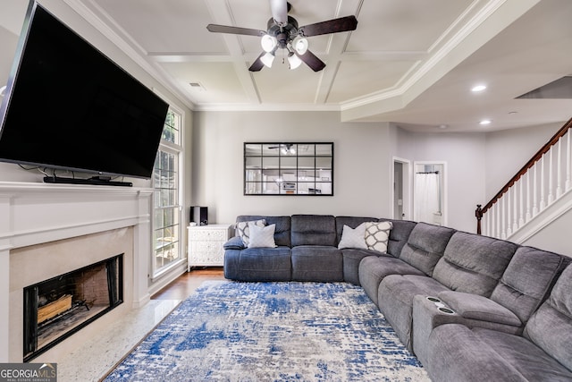 living area featuring crown molding, ceiling fan, stairway, a fireplace, and coffered ceiling