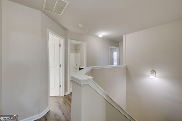 hall featuring baseboards, visible vents, wood finished floors, and an upstairs landing