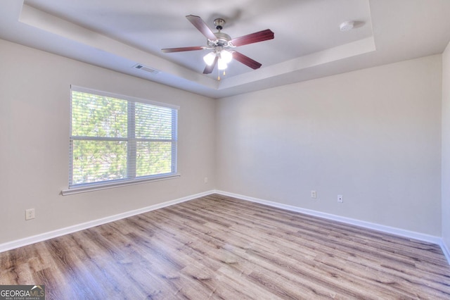 empty room featuring visible vents, a raised ceiling, and wood finished floors