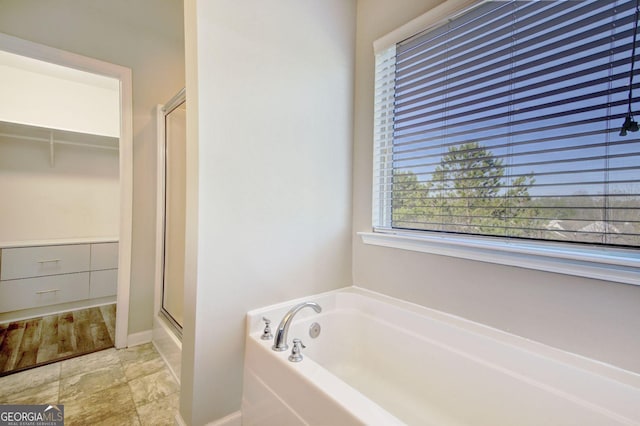 full bath featuring a stall shower, a walk in closet, a garden tub, and baseboards