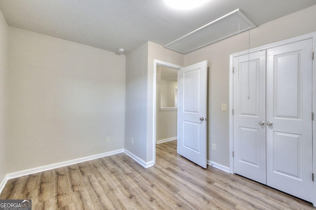 unfurnished bedroom featuring light wood-style floors, attic access, baseboards, and a closet