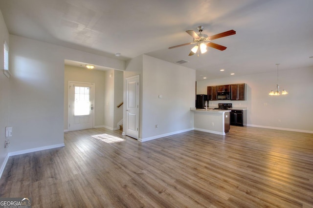 unfurnished living room featuring ceiling fan with notable chandelier, visible vents, wood finished floors, baseboards, and stairs