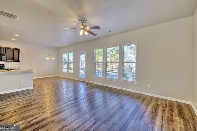 unfurnished living room featuring ceiling fan with notable chandelier, dark wood-type flooring, a sink, visible vents, and baseboards