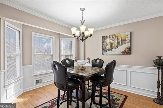 dining room featuring light wood-style floors, a notable chandelier, plenty of natural light, and ornamental molding