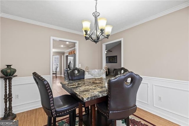 dining space featuring a notable chandelier, a decorative wall, ornamental molding, wainscoting, and wood finished floors