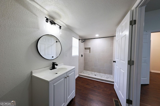 full bathroom featuring a textured ceiling, wood finished floors, vanity, visible vents, and tiled shower