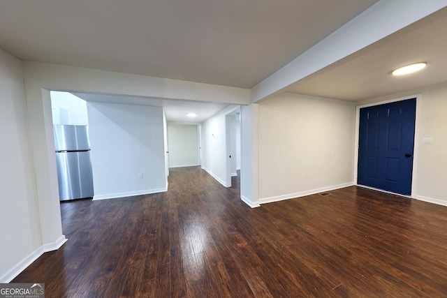 finished below grade area with dark wood-style floors, freestanding refrigerator, and baseboards