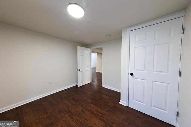 unfurnished bedroom with dark wood-style floors, visible vents, and baseboards