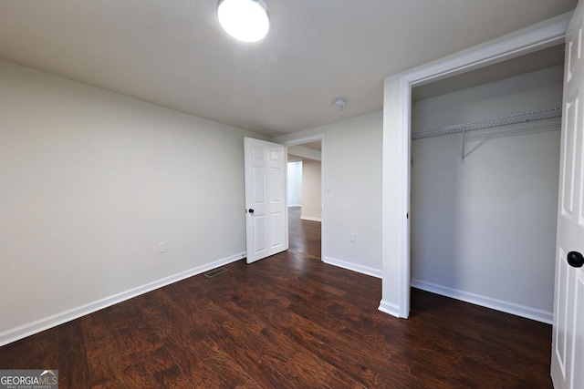 unfurnished bedroom with a closet, dark wood-style flooring, visible vents, and baseboards