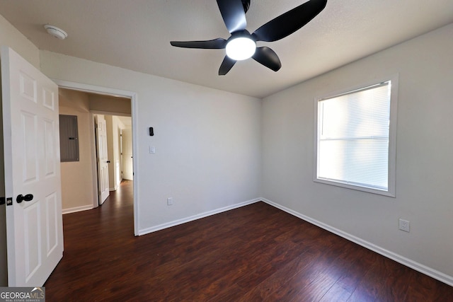 spare room featuring a ceiling fan, electric panel, baseboards, and dark wood-type flooring