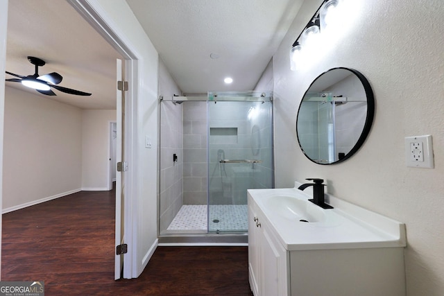 full bathroom featuring ceiling fan, wood finished floors, vanity, baseboards, and a shower stall