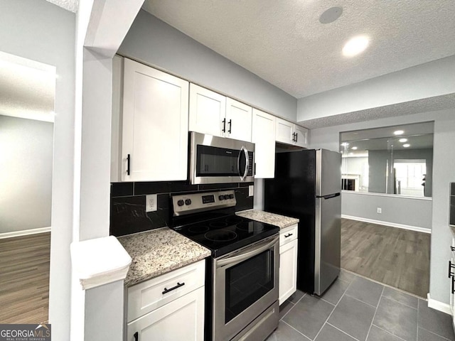 kitchen with decorative backsplash, light stone countertops, stainless steel appliances, a textured ceiling, and white cabinetry