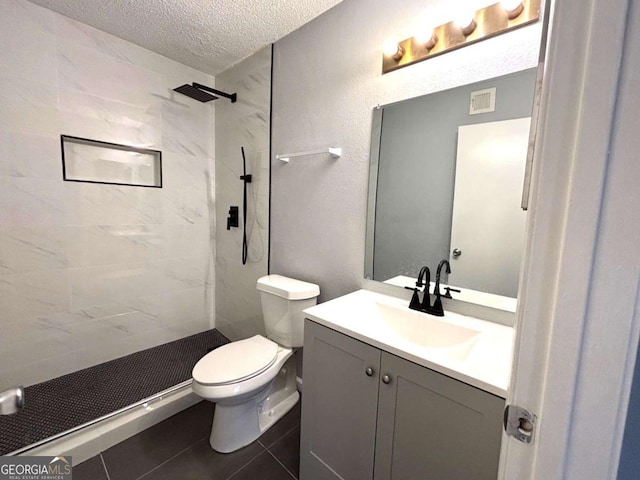 bathroom featuring toilet, tile patterned flooring, a tile shower, a textured ceiling, and vanity