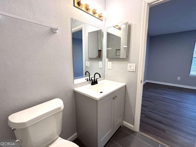 bathroom with toilet, vanity, baseboards, and a textured wall