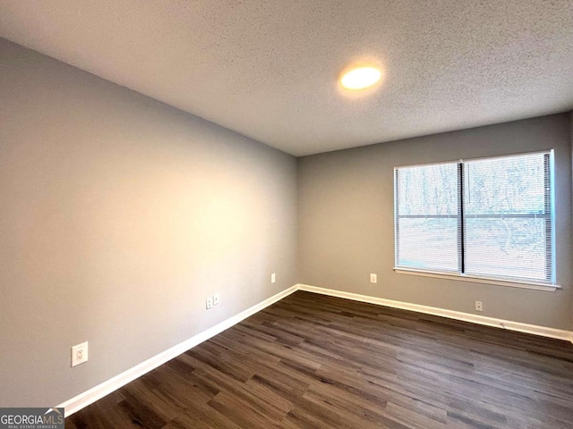 spare room with a textured ceiling, baseboards, and dark wood-type flooring